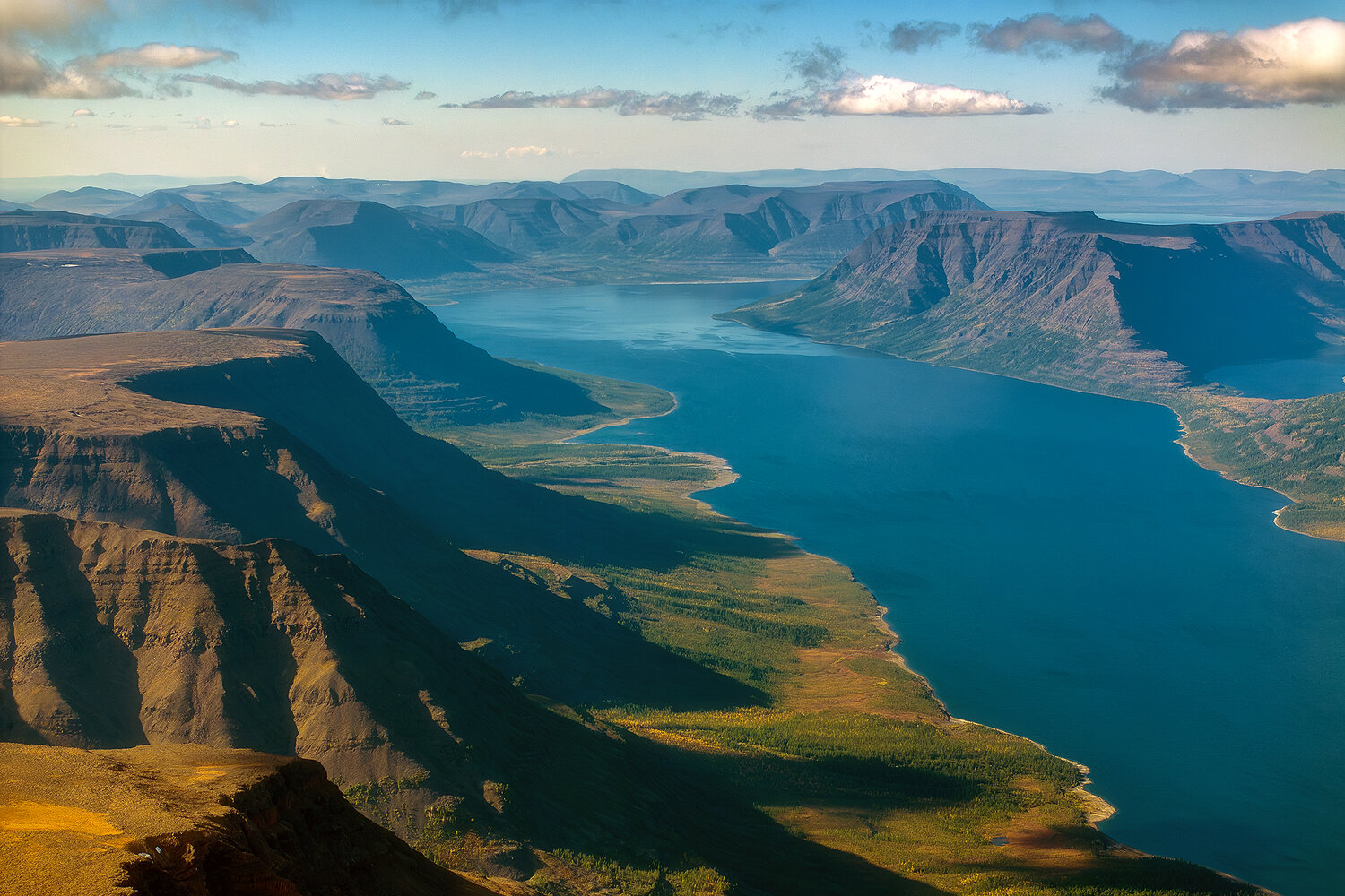 A deep blue lake winding between dramatic flat-topped mountains beneath scattered clouds